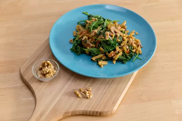 Hello Fresh - Herbstliche Grünkohl-Spätzle-Pfanne in cremiger Soße mit gerösteten Walnüssen auf einem blauen Teller auf einem Holzbrett