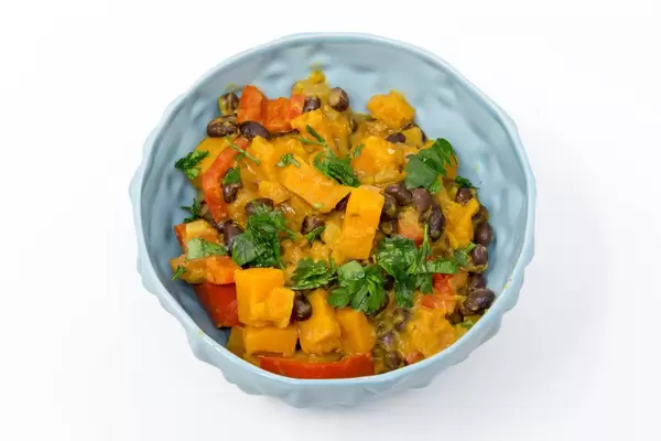 Hello Fresh - Karibischer Süßkartoffel-Kokos-Eintopf mit Bohnen in blauer Schüssel auf weißem Hintergrund - Nahaufnahme