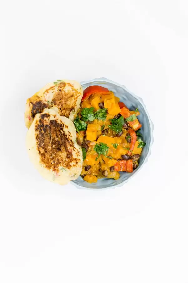 Hello Fresh - Karibischer Süßkartoffel-Kokos-Eintopf mit Bohnen und herzhaften Bananenpfannkuchen in blauer Schüssel auf weißem Hintergrund - Aufsicht