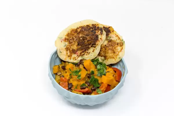 Hello Fresh - Karibischer Süßkartoffel-Kokos-Eintopf mit Bohnen und herzhaften Bananenpfannkuchen in blauer Schüssel auf weißem Hintergrund