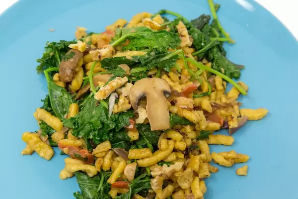 Hello Fresh Spätzle Noodles with kale and mushrooms in creamy sauce with roasted walnuts on a blue plate - close up