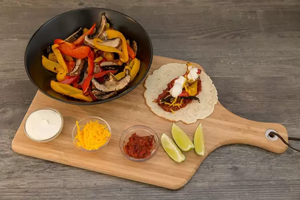 Hello Fresh - Vegetarische Fajitas mit Paprika & Pilzen selbst gemachter, scharfer Soße und Limettenschmand auf einem Brettchen