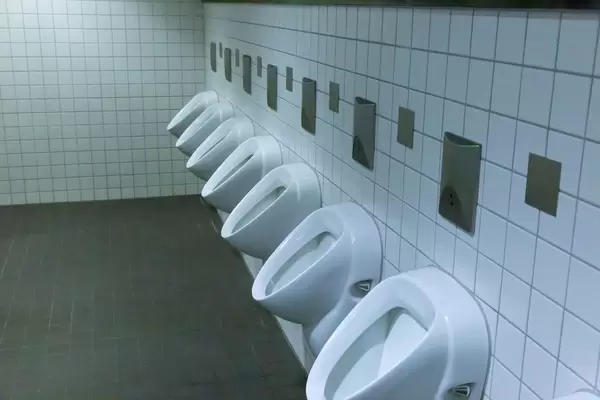 Herrentoilette mit mehreren Pissoire in einer Reihe an gefliester Wand