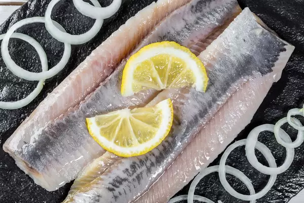Herring fillet with onion and lemon on black stone. Top view