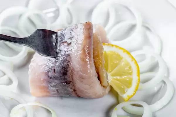 Herring with sliced onion and lemon on white ceramic plate