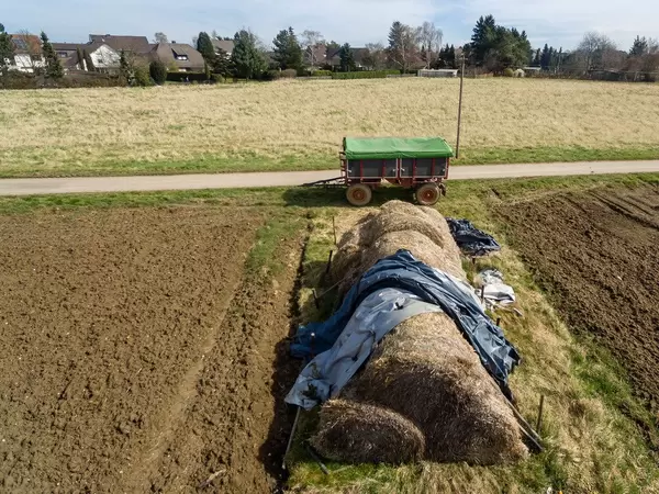 Heuhaufen zwischen bestellten Feldern und ein Anhänger im Hintergrund - Drohnenaufnahme