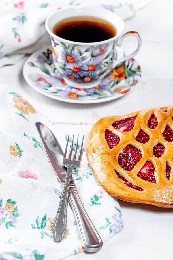 Himbeerkuchen mit einer Tasse Tee und Besteck auf dem gedeckten Tisch