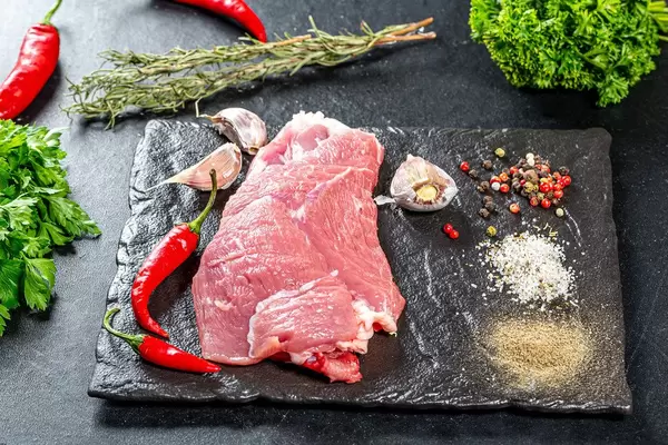 Hintergrundbild mit Zutaten zum Kochen: rohes Fleisch, Chilischoten, Knoblauchzehen, Kräuter und farbenfrohe Gewürze