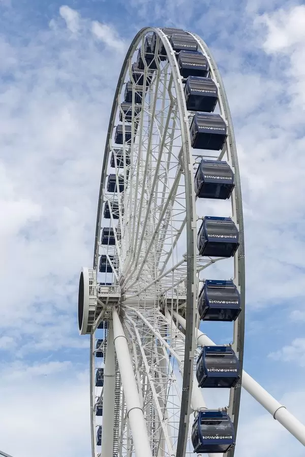Hohes, weißes Riesenrad mit blauen Kabinen vor bewölktem Himmel