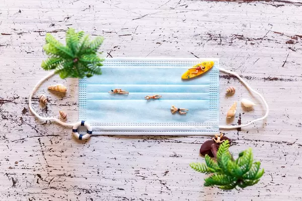 Holiday at the beach during a pandemic: face mask with miniature figures swimming and surfing on it