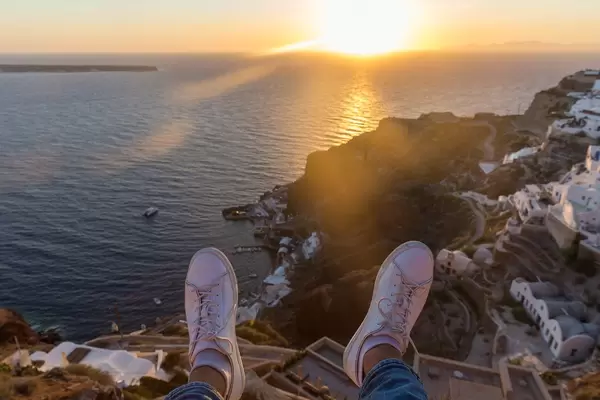 Holiday feeling in Greece: feet of a man watching the sunset and enjoying the views of Santorini