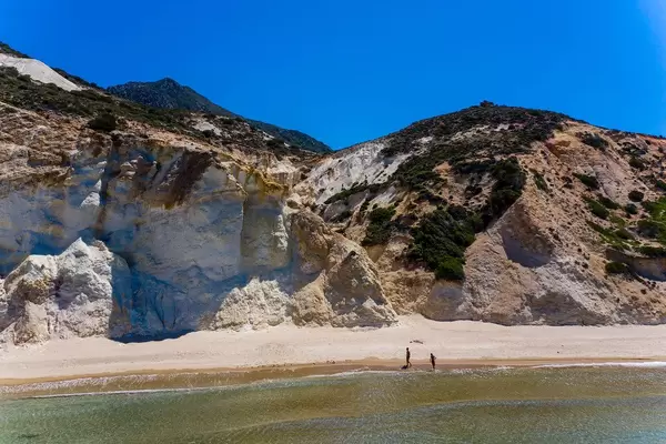 Holiday in Greece: almost deserted beach with just two people walking in the sun on the island of Milos