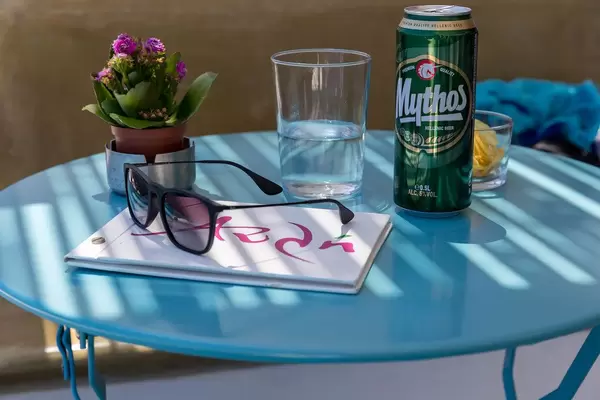 Holiday in Greece: sunglasses, flowers, a can of Mythos beer, water and menu on a blue table