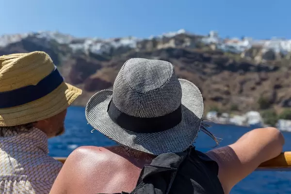 Holiday in Greece: tourists wear hats protecting them from the scorching sun, seen from the back