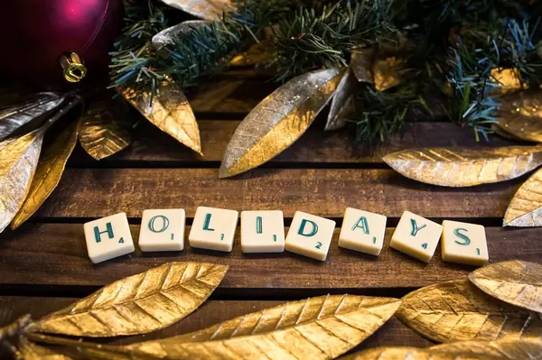 HOLIDAYS - buchstabiert auf hölzernem Untergrund mit Goldenen Blättern und Tannenzweigen