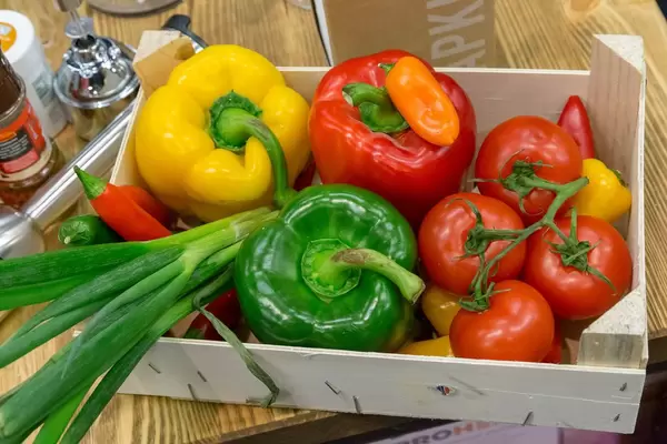 Hölzerne Kiste gefüllt mit Gemüse wie Paprika, Tomaten, Lauch und Chilis auf Holztisch