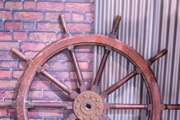 Hölzernes, antikes Steuerrad von altem Boot vor Backsteinmauer und Wellblech