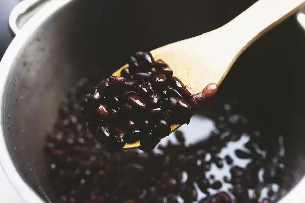 Holzlöffel mit gekochten schwarzen Bohnen über Kochtopf