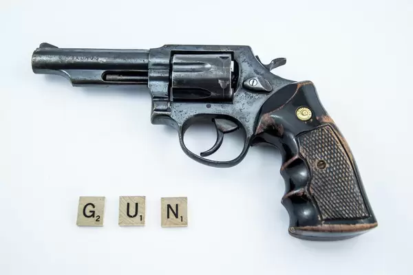 Holzplättchen mit Buchstaben bilden das Wort GUN neben Waffe auf weiße Hintergrund