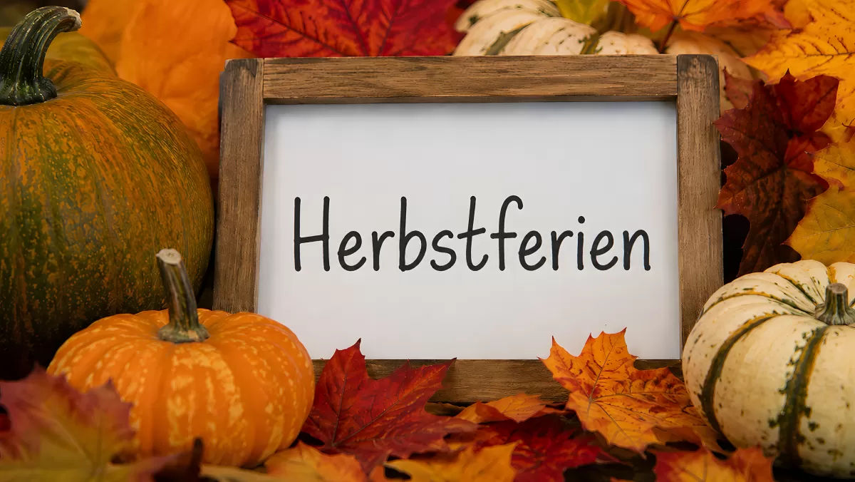 Holzschild mit Herbstferien-Aufschrift zwischen Kürbissen