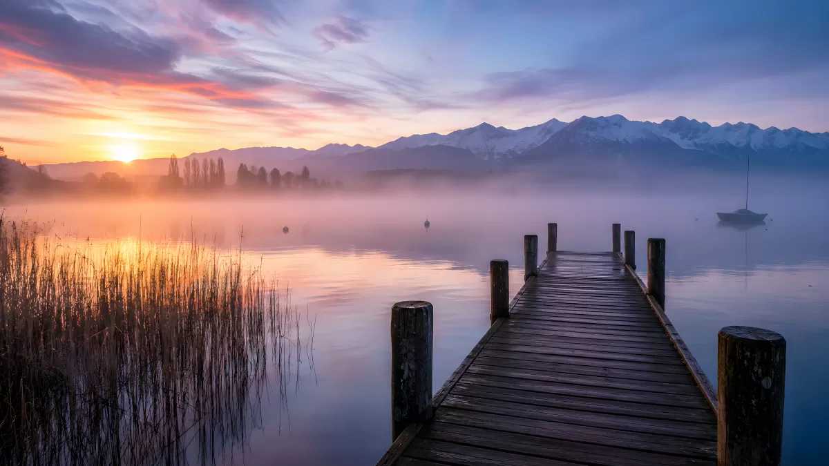 Holzsteg am Bergsee bei nebligem Sonnenaufgang
