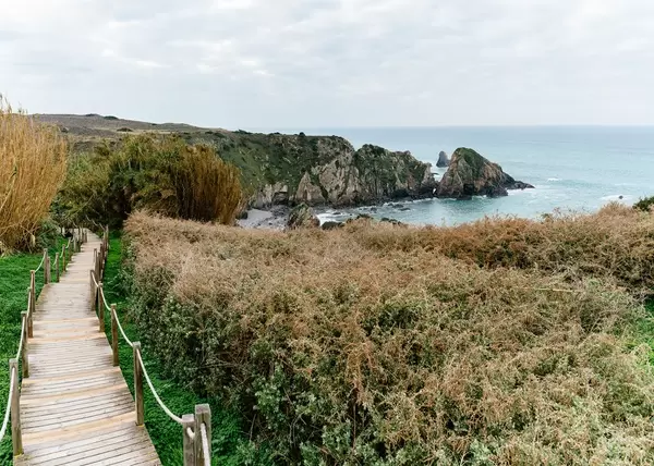 Holzsteg führt durch grüne Umgebung zu felsigem Strand bei Vila do Bispo, Portugal