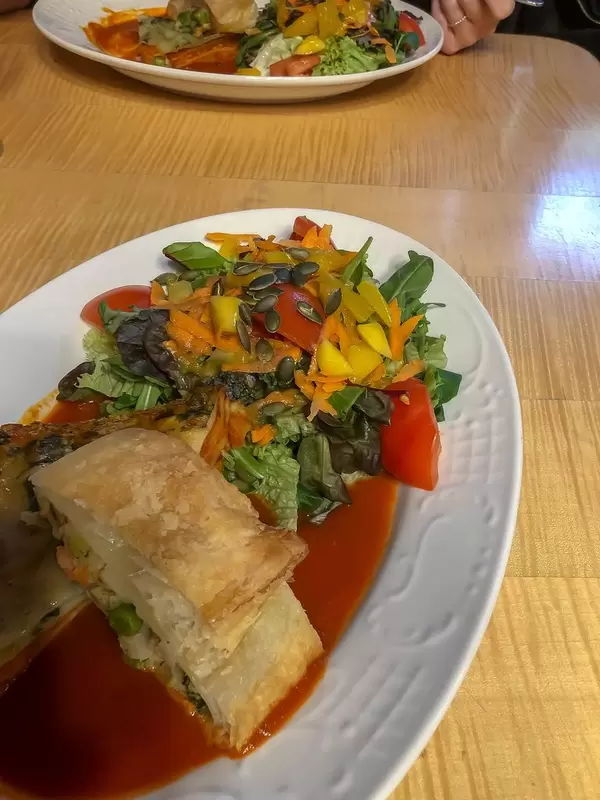Holztisch mit zwei Tellern mit Gemüselasagne und grünem Salat in Tomatensoße