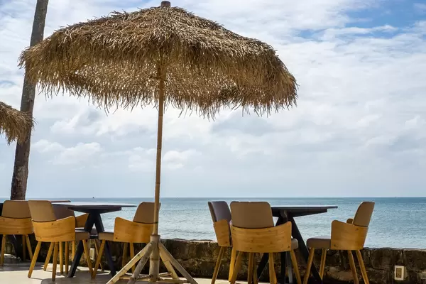 Holztische, Holzstühle und Sonnenschirm aus Palmenblättern bei einer Strandbar mit Aussicht auf das Meer in Phu Quoc, Vietnam