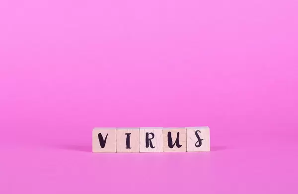 Holzwürfel mit dem Wort Virus vor pinkem Hintergrund