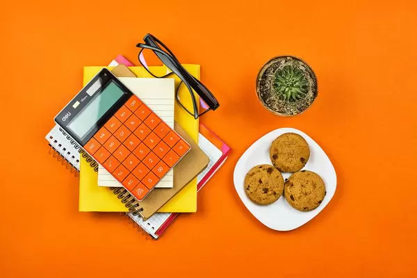 Home office. Notepad, calculator, cactus and cookies on orange background