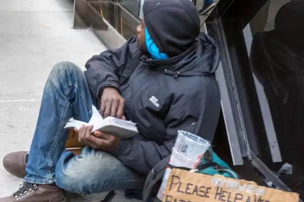 Homeless man sitting on the street, reading a book and begging for money