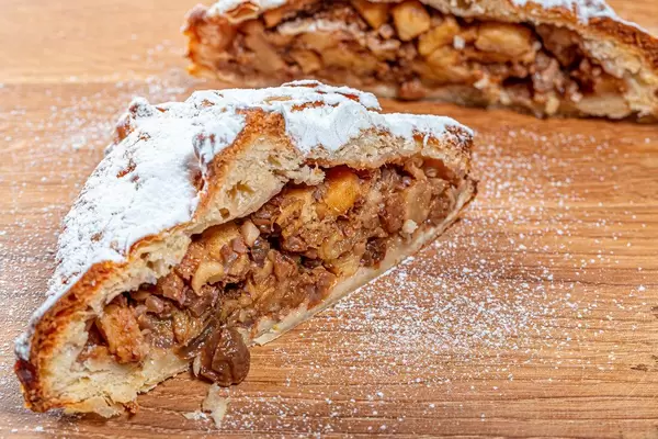 Homemade apple strudel with apples, nuts and powdered sugar on wooden background