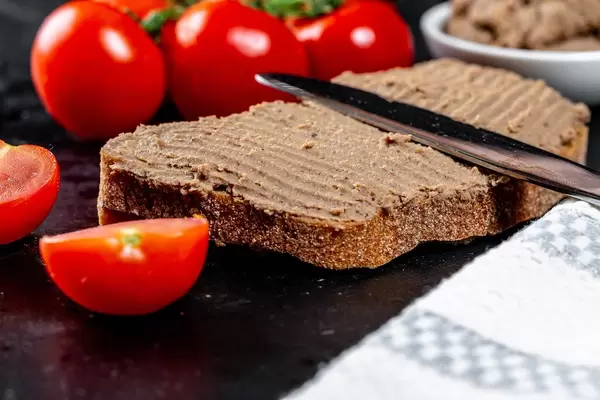 Homemade chicken liver pate on baguette and in white bowl with tomatoes