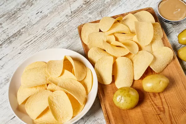 Homemade fresh chips and young raw potatoes on the cutting board
