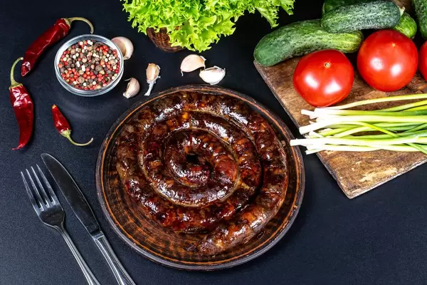 Homemade sausage with spices and vegetables on black background