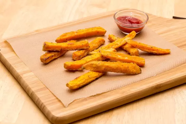 Homemade sweet potato fries on a cutting board with tomato ketchup next to it
