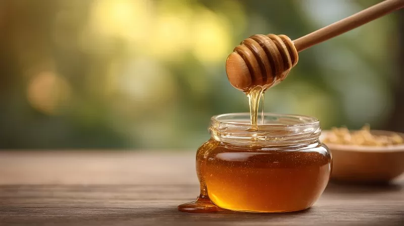 Honig fließt von Löffel in Glas bei Tageslicht