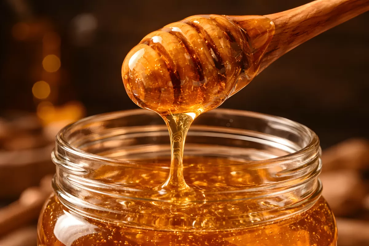 Honig tropft vom Holzlöffel in ein Glasgefäß