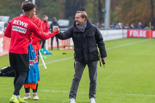 Horst Heldt klatscht die Spieler beim Training ab auf dem Rasen