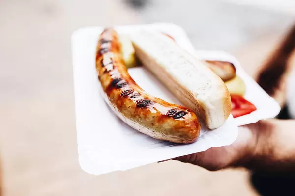 Hot dog: man serves a sausage with long bread and mustard on a cardboard tray