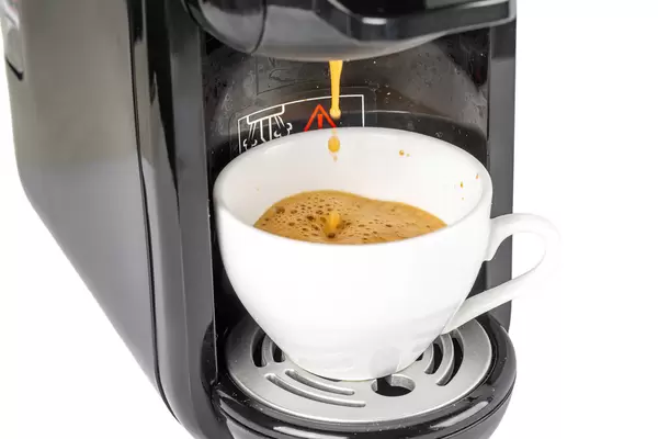 Hot espresso coffee is poured into the cup from the coffee machine, close-up