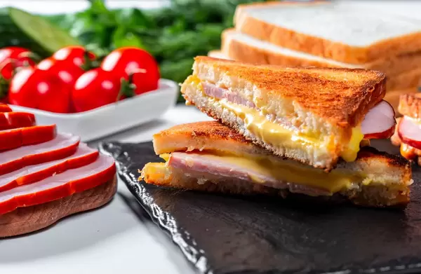 Hot ham and cheese sandwiches with tomatoes and herbs in the background