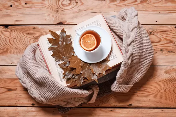 Hot lemon tea, book and autumn leaves with knitted sweater on rustic wood