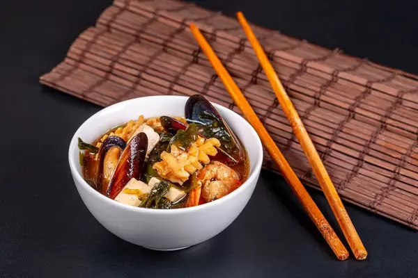 Hot miso soup with seafood in white bowl on dark background