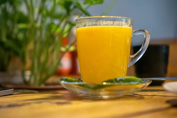 Hot Orange Tea with Cinammon in a Glass Cup with Plants in the Background