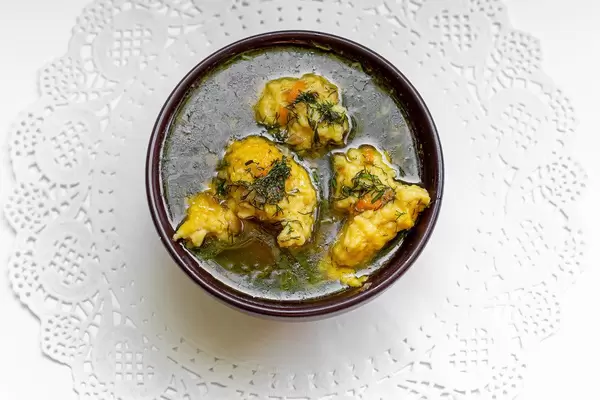 Hot soup with dumplings in a brown bowl on a white lace napkin