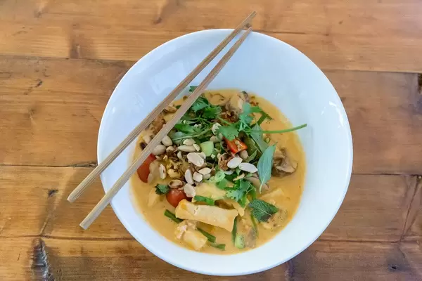 Hot, vegan organic Tofu Pho-sot cari in red coconut curry from Chum Chay Restaurant, with bush beans, oyster mushrooms & cashew nuts on a wooden table