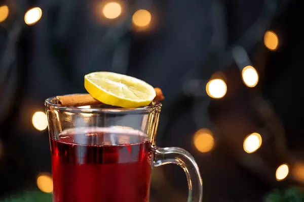 Hot wine with a sliced orange and cinnamon in the front and warm lights in the background