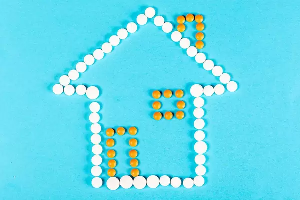 House made of pills on a blue background. The concept of being treated at home