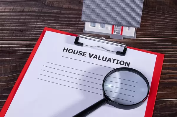 House valuation document with small family house and magnifying glass on wooden table
